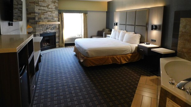 Habitación de hotel con una cama grande, televisión de pantalla plana, chimenea, escritorio y baño con bañera y lavabo.