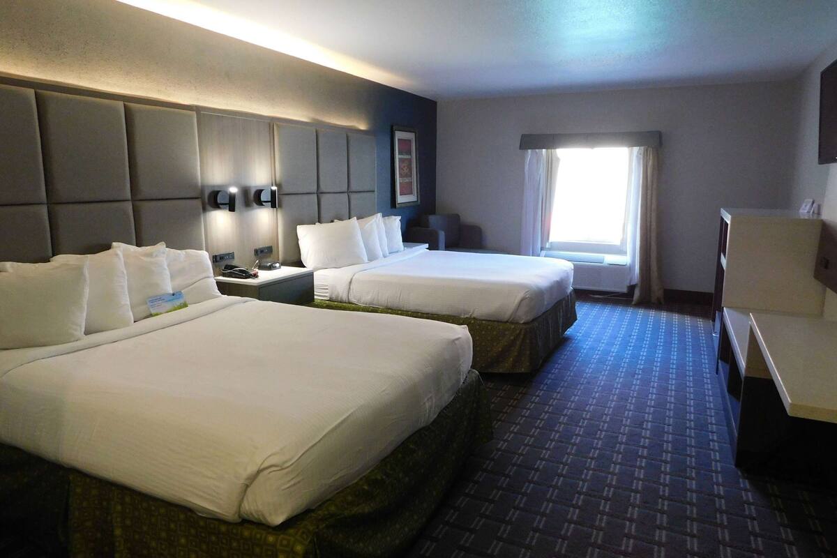 A hotel room with two beds, a desk, a chair, a window with curtains, and a wall-mounted phone.
