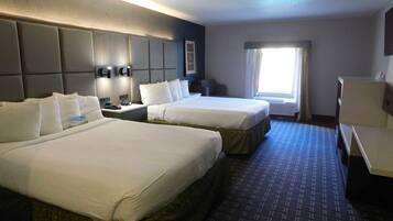 A hotel room with two beds, a desk, a chair, a window with curtains, and a wall-mounted phone.