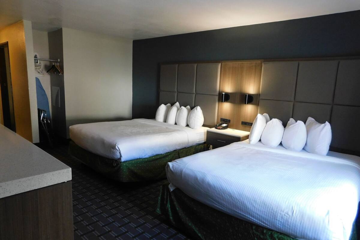 A hotel room with two beds, a desk, and a headboard with built-in lighting.