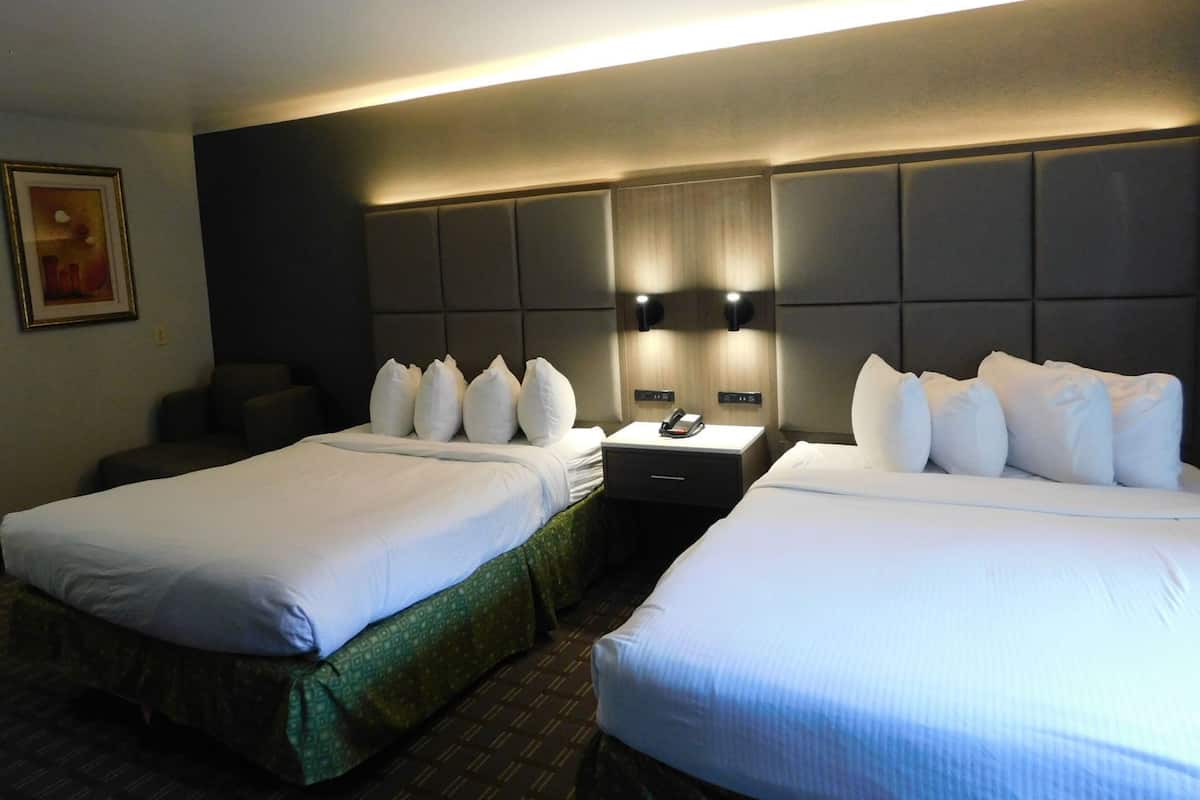 A hotel room with two beds, a nightstand, a telephone, and a wall-mounted light fixture.
