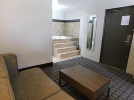 A hotel room with a sofa, a wooden table, a mirror, and a door.