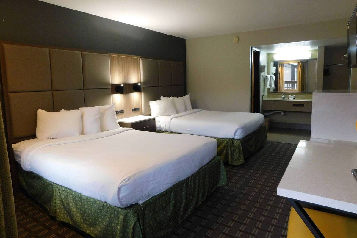 A hotel room with two beds, a large mirror, a small table, and a bathroom visible through an open door.
