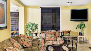 Una sala de estar con sofá, sillón, mesa de centro, televisor de pantalla plana y dos plantas en macetas.