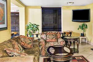Una sala de estar con sofá, sillón, mesa de centro, televisor de pantalla plana y dos plantas en macetas.