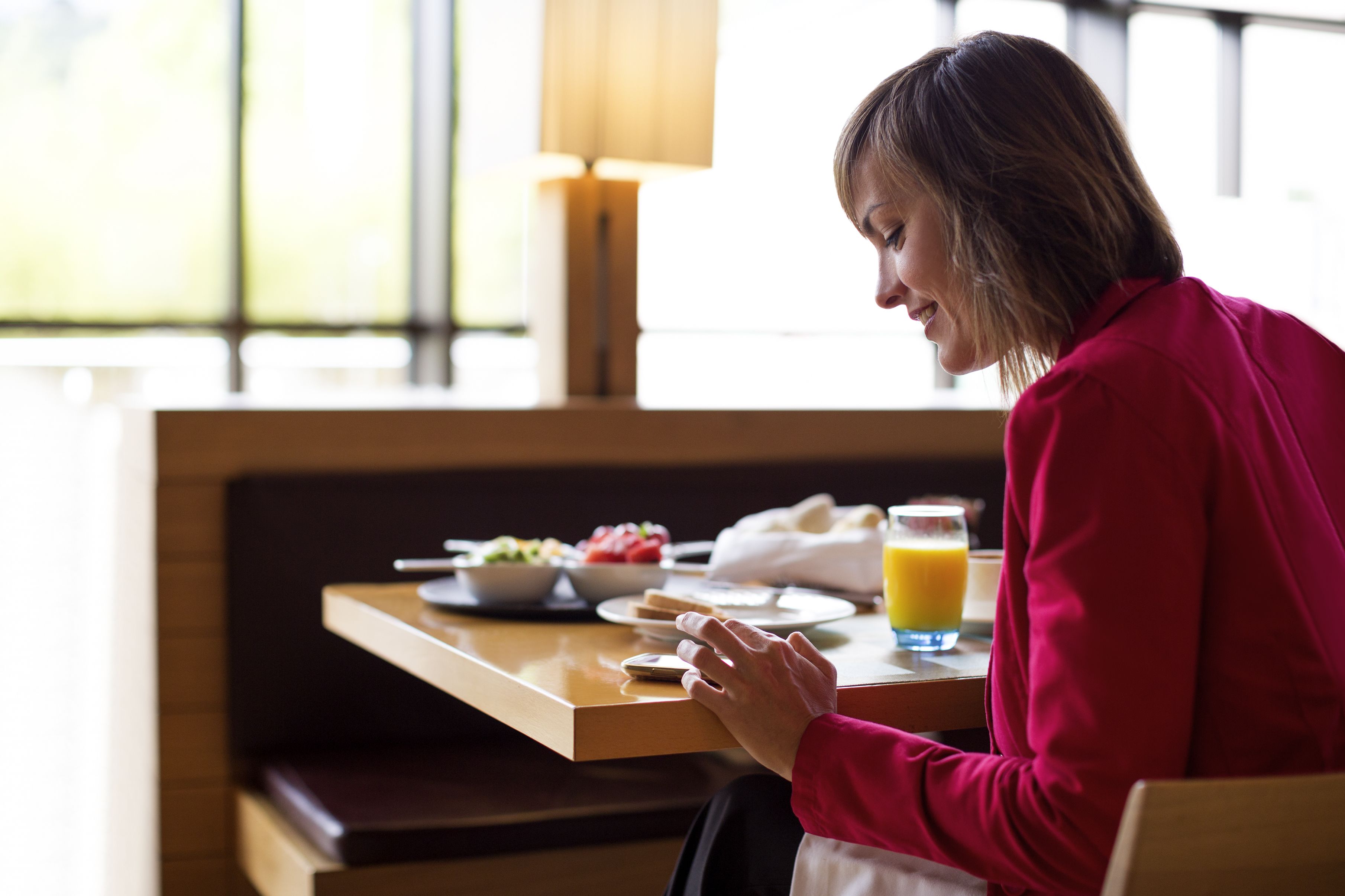 Una persona sentada a una mesa con alimentos para el desayuno, incluyendo un tazón de fruta, un vaso de jugo de naranja y un plato de comida.