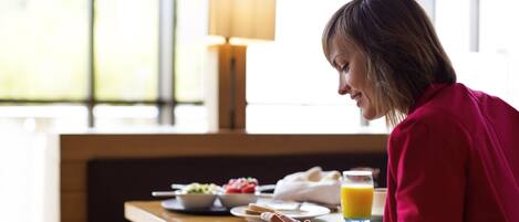 Una persona sentada a una mesa con alimentos para el desayuno, incluyendo un tazón de fruta, un vaso de jugo de naranja y un plato de comida.