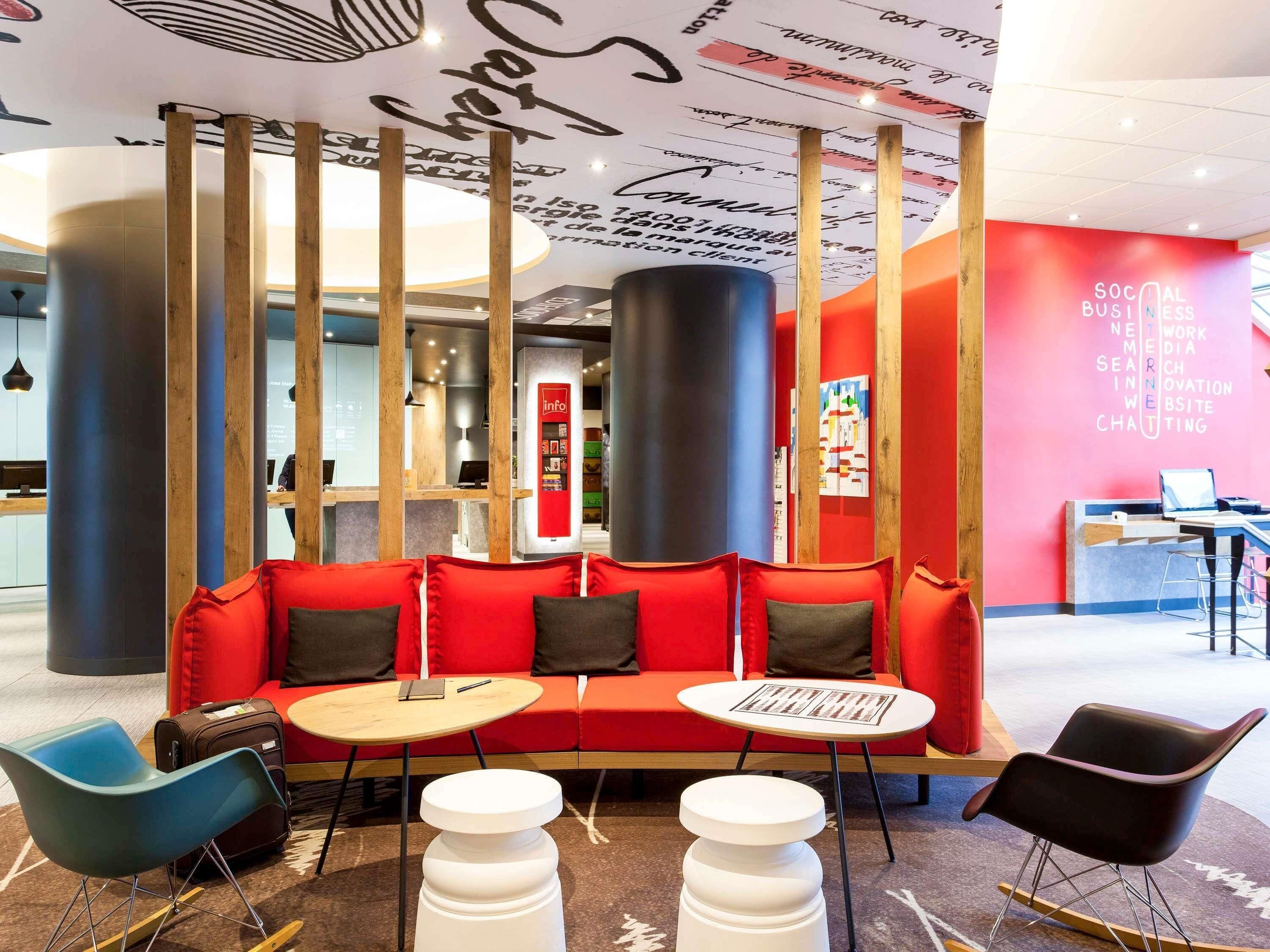 A modern lounge area with a red sofa, two white tables, and a blue chair.