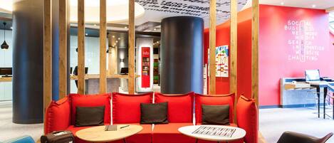 A modern lounge area with a red sofa, two white tables, and a blue chair.