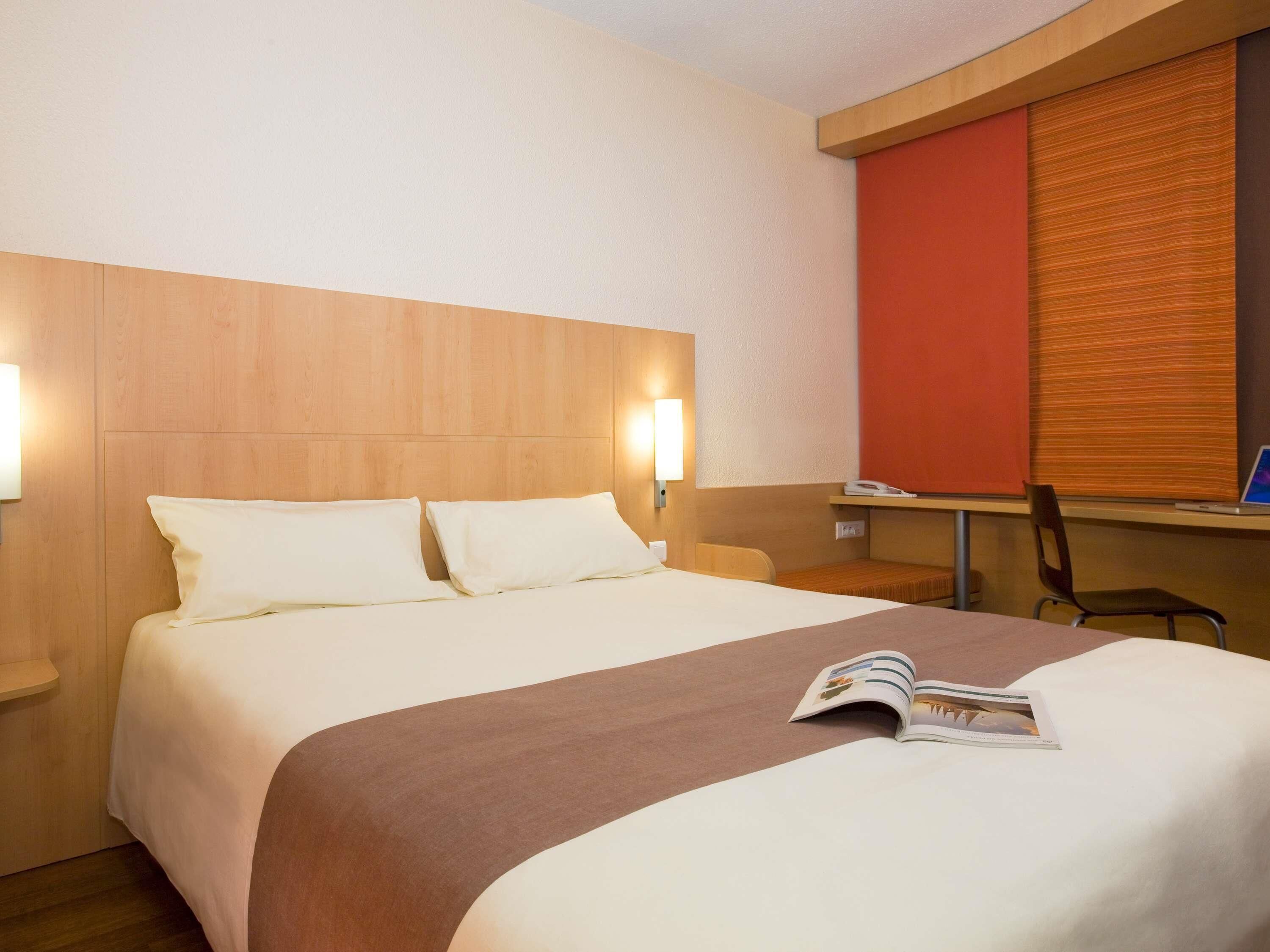 A hotel room with a bed, bedside lamps, a desk, and a chair.