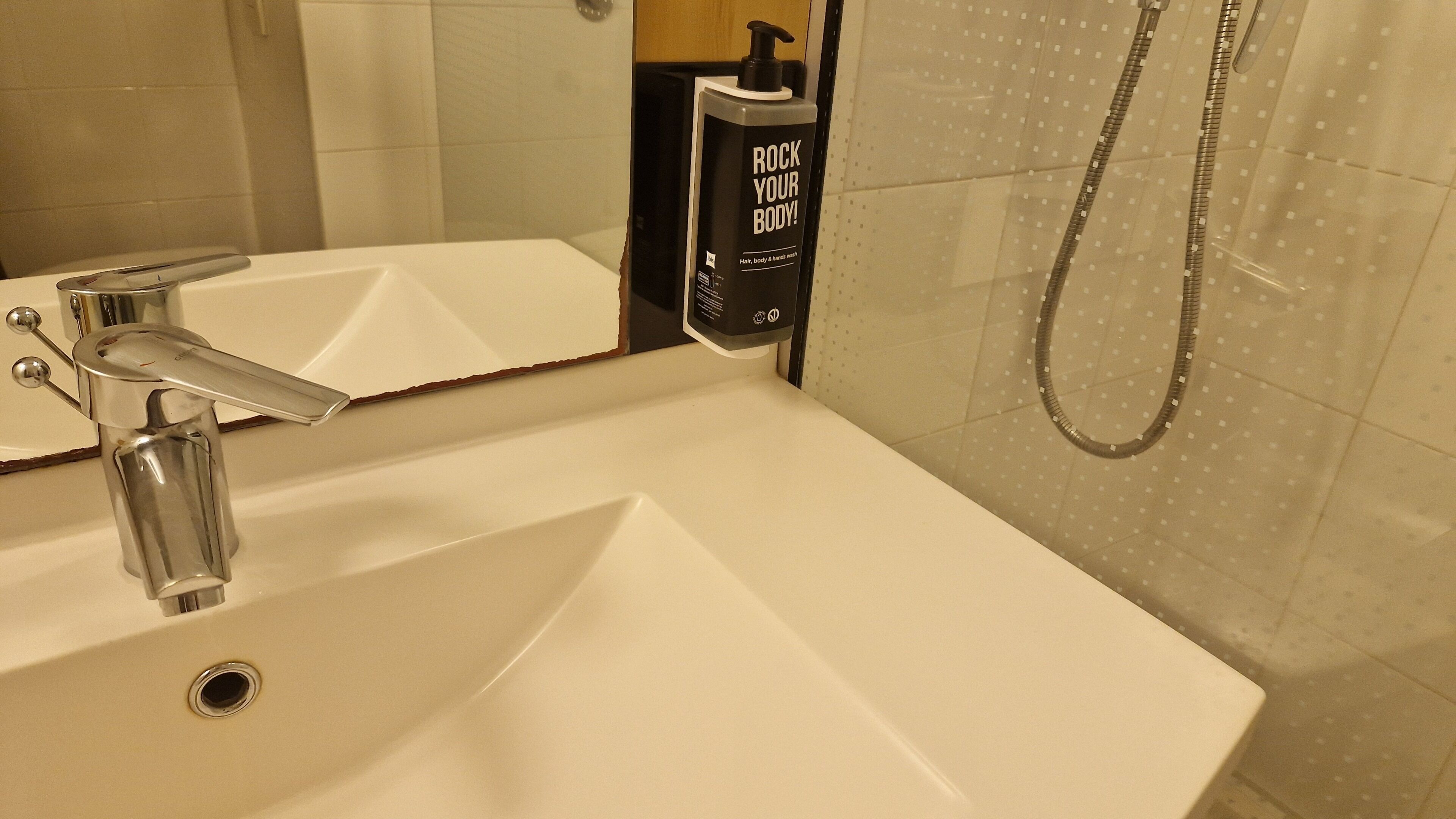 A bathroom with a white sink, a modern faucet, a handheld showerhead, and a bottle of body wash.