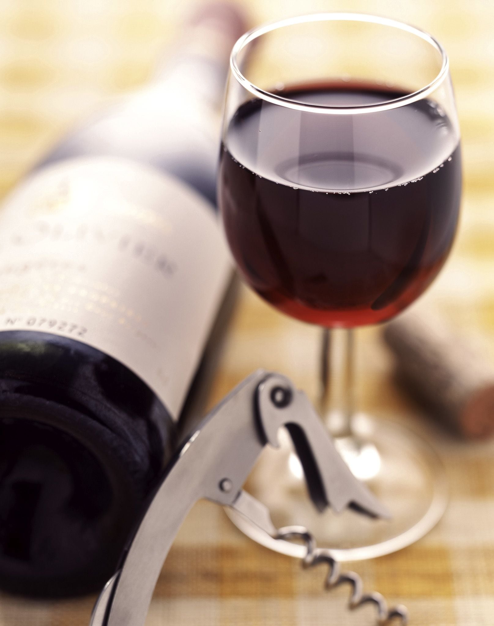 A bottle of wine, a wine glass, and a corkscrew on a table.