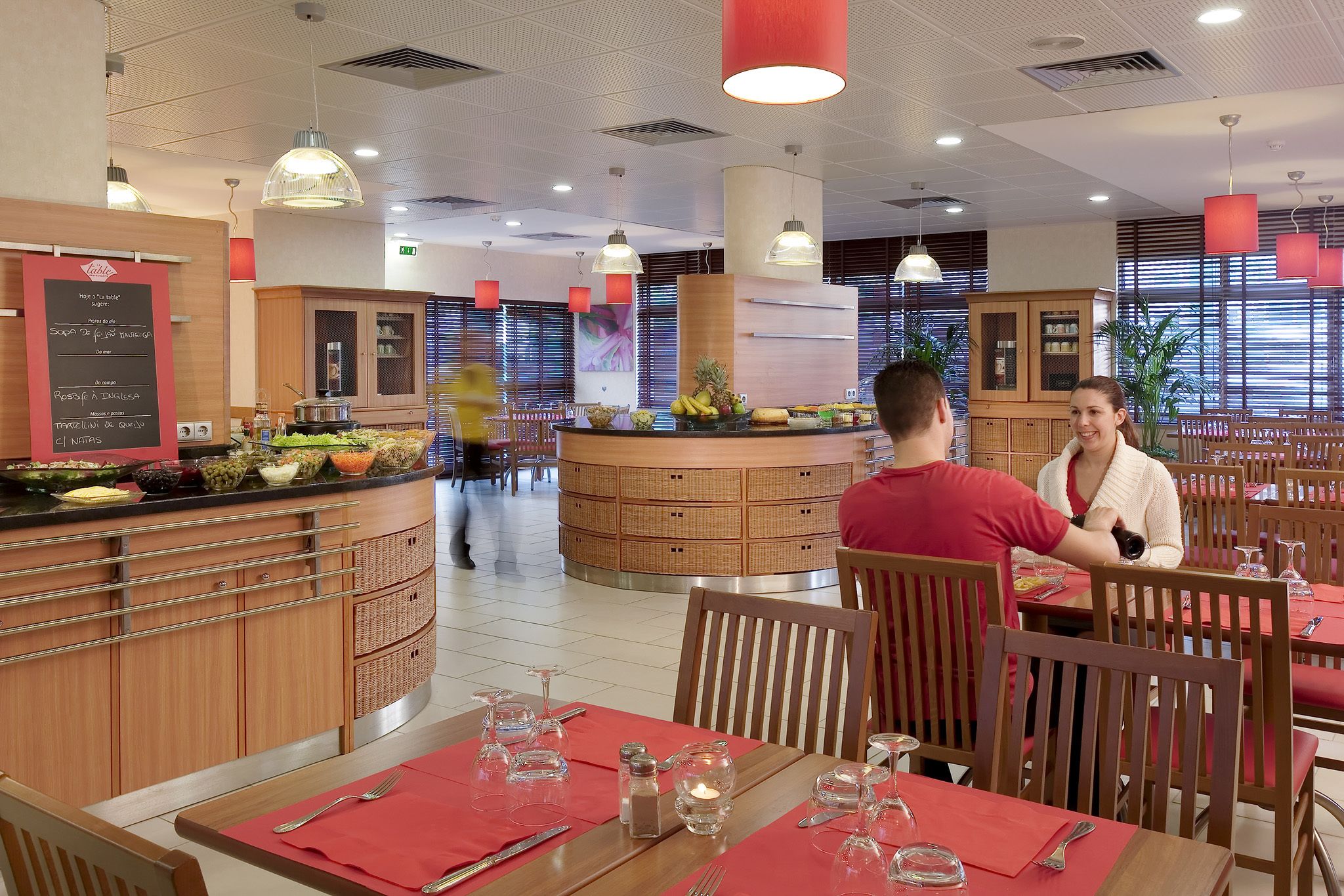 A modern restaurant with wooden furniture, a central counter with fresh fruits, and a bright interior.