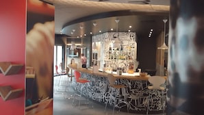 A bar area with a curved counter, multiple stools, and a wall with abstract art. - ibis Lisboa José Malhoa (Lisbon)
