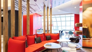 A modern lounge area with red seating, a small table, and a large window. - ibis Lisboa José Malhoa (Lisbon)