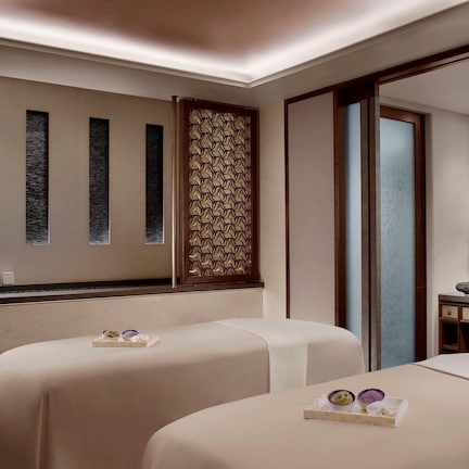 A hotel room with two beds, a vanity with a mirror, and a decorative wall panel.