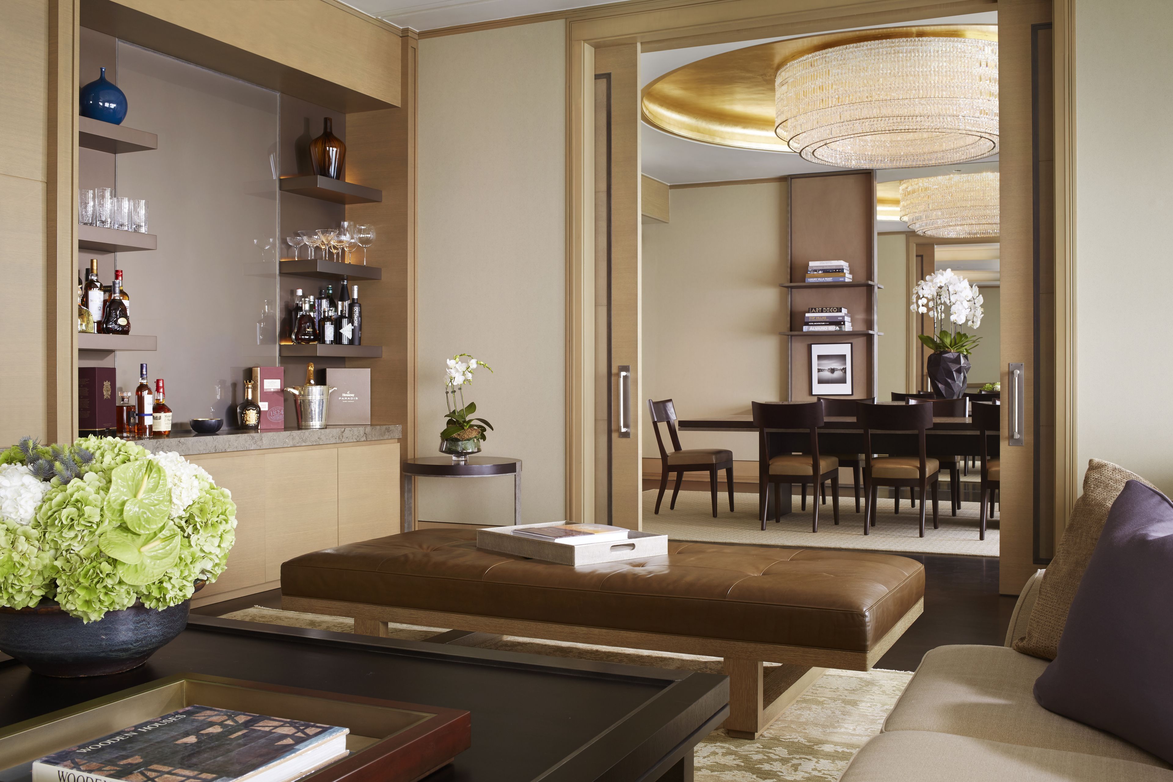 Un salon moderne avec un canapé en cuir marron, une table basse et un coin repas agrémenté d’un lustre.