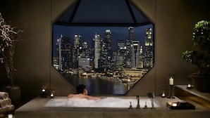A man relaxing in a bathtub with a cityscape view through a large window. - The Ritz-Carlton, Millenia Singapore (Singapore)