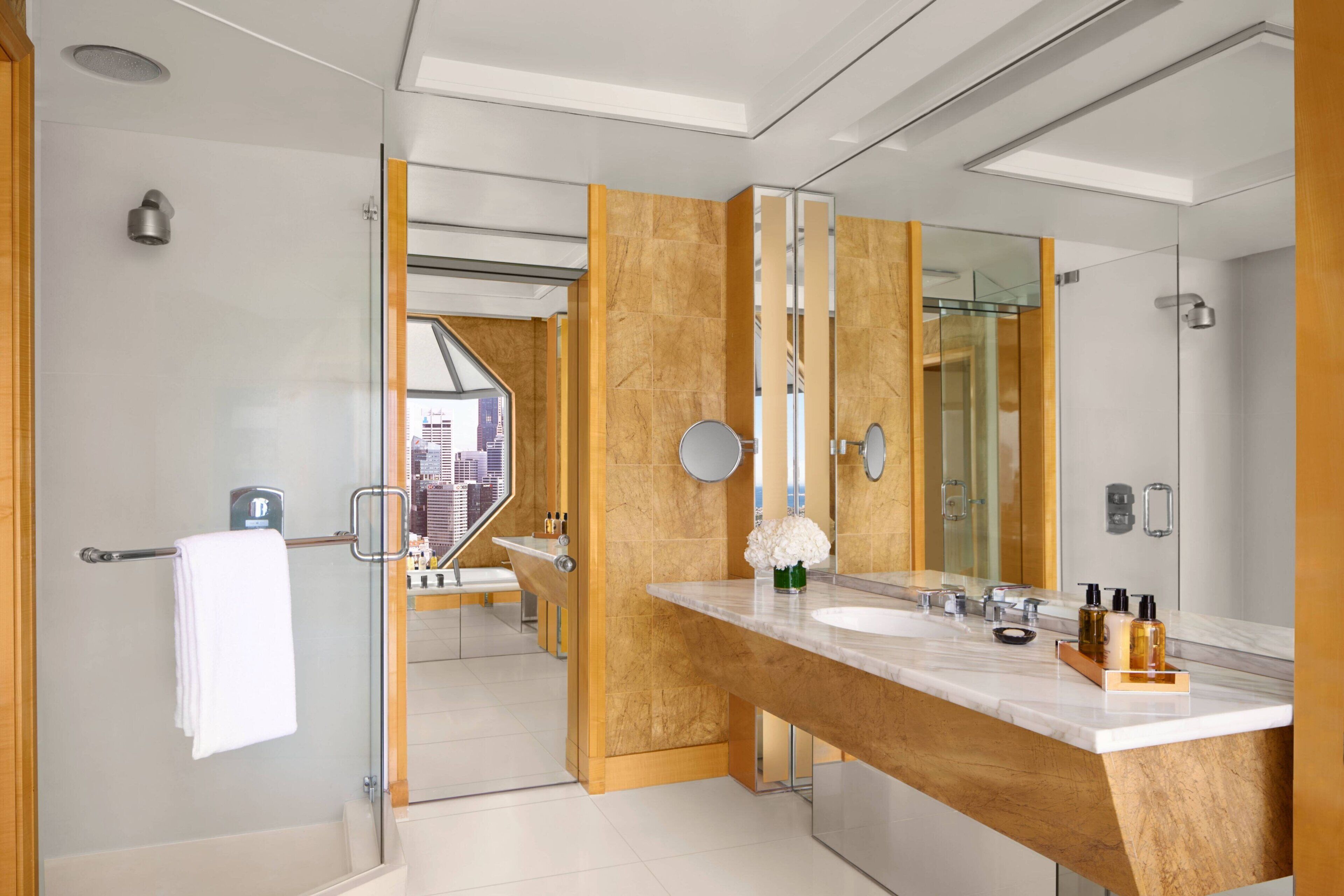 Een moderne badkamer met een grote spiegel, twee wastafels en uitzicht op een stadsbeeld door een glazen deur.