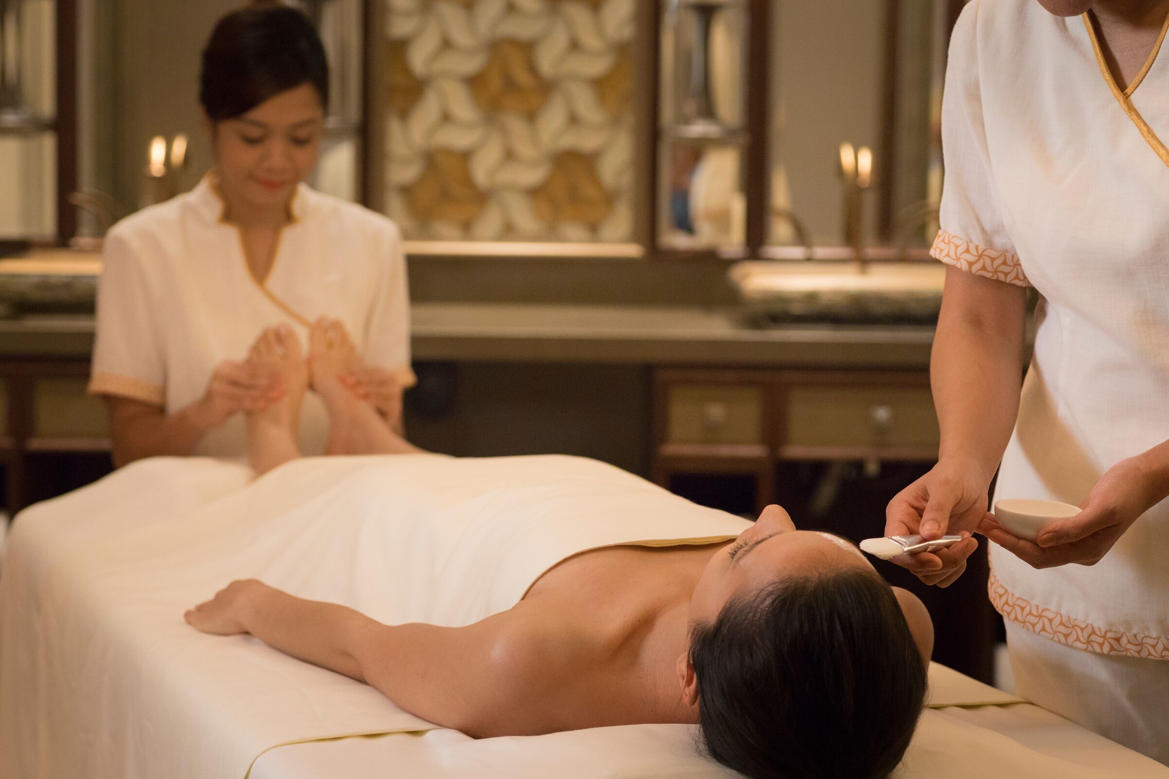 Sesión de masoterapia en un spa, con un cliente recostado en la camilla, un terapeuta aplicando el tratamiento y otra persona atendiendo al cliente.