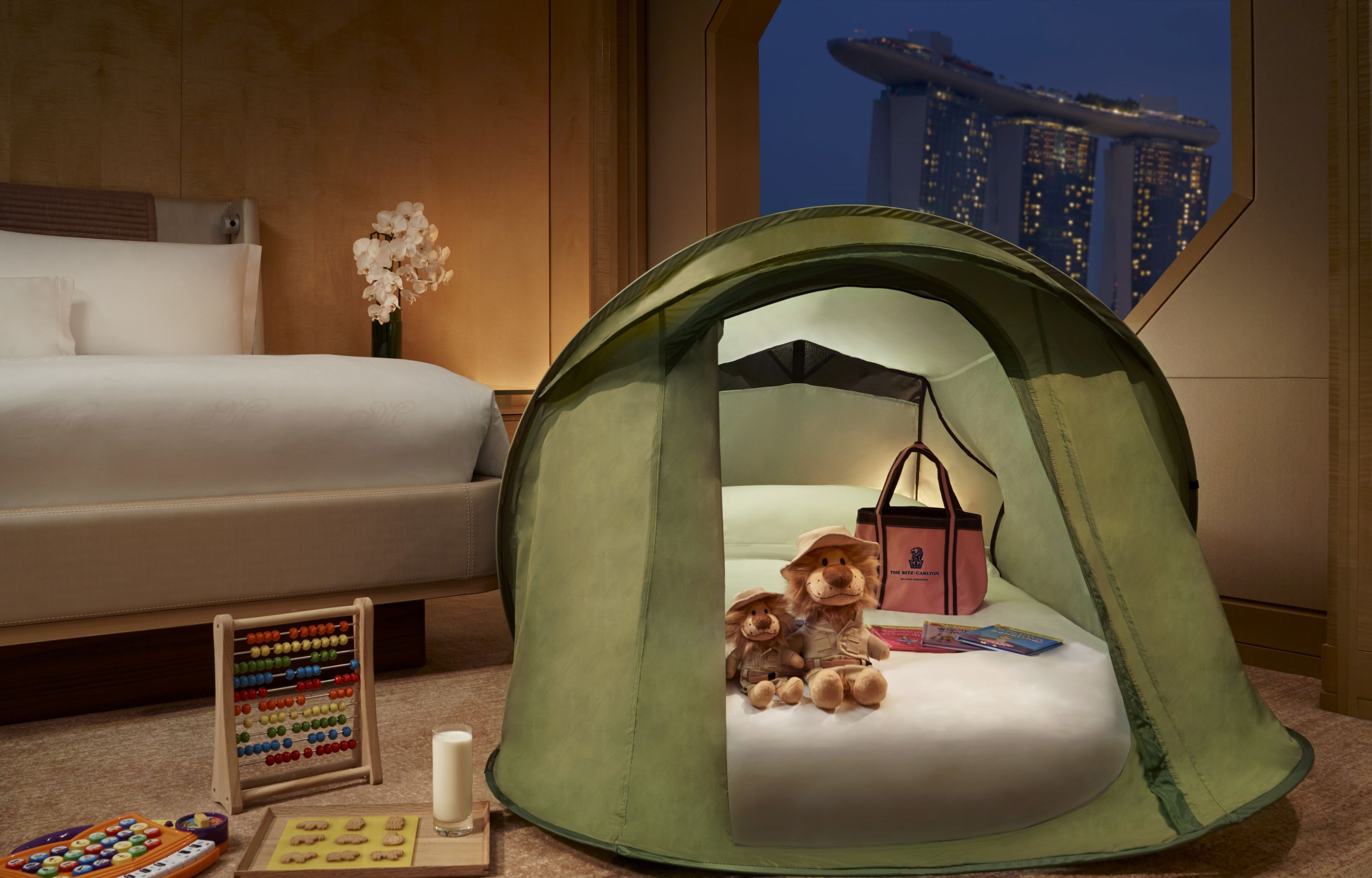 A bedroom with a green tent-like structure containing teddy bears, a small table with a teddy bear, a toy abacus, and a candle.
