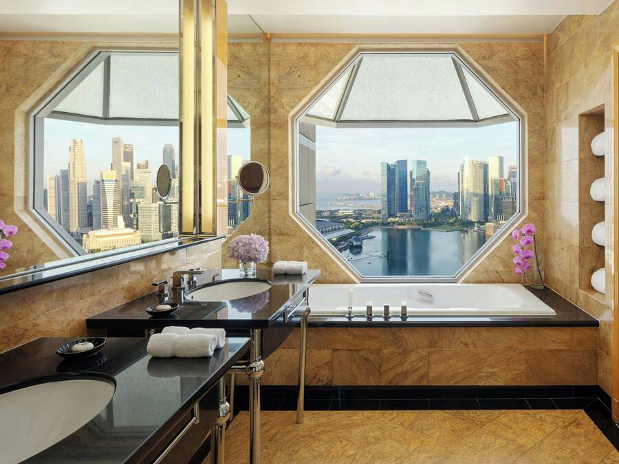 Un baño moderno con una bañera grande, lavamanos doble y vistas a la ciudad a través de amplias ventanas.