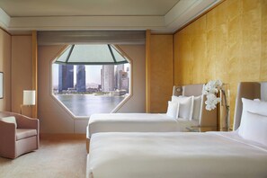 A hotel room with a large window, two beds, a chair, and a view of a cityscape.