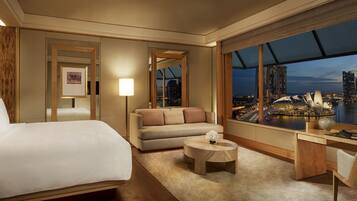 A hotel room with a large bed, a sofa, a desk, and a view of a cityscape.