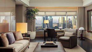 A modern hotel room with a city view, a sofa, a chair, a desk, and a lamp. - The Ritz-Carlton, Millenia Singapore (Singapore)