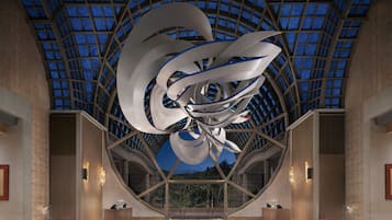 A modern interior with a large, abstract sculpture in the center, a glass ceiling, and a reception desk with a view outside.