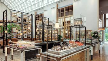 Un amplio atrium con techos altos y luz natural, que presenta una mesa central con diversos alimentos y está rodeado de estanterías con cuadros y objetos decorativos.