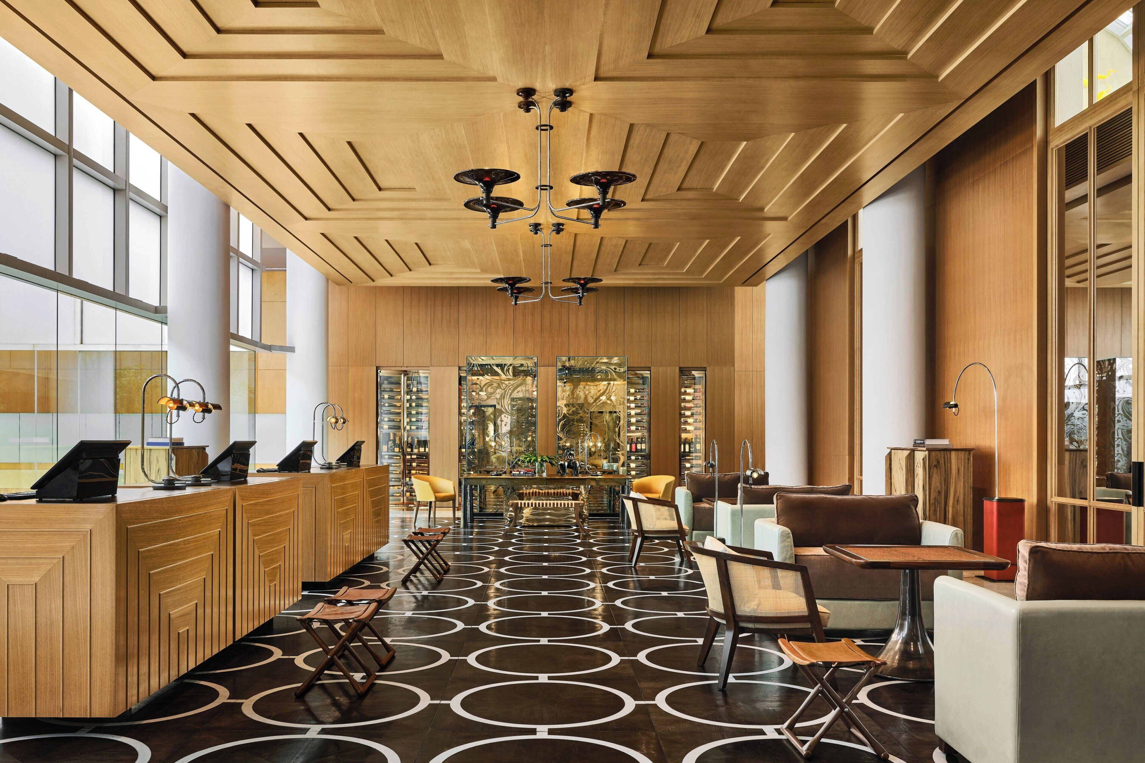 En moderne hotellobby med en træreception, siddeområde og et mønstret gulv.