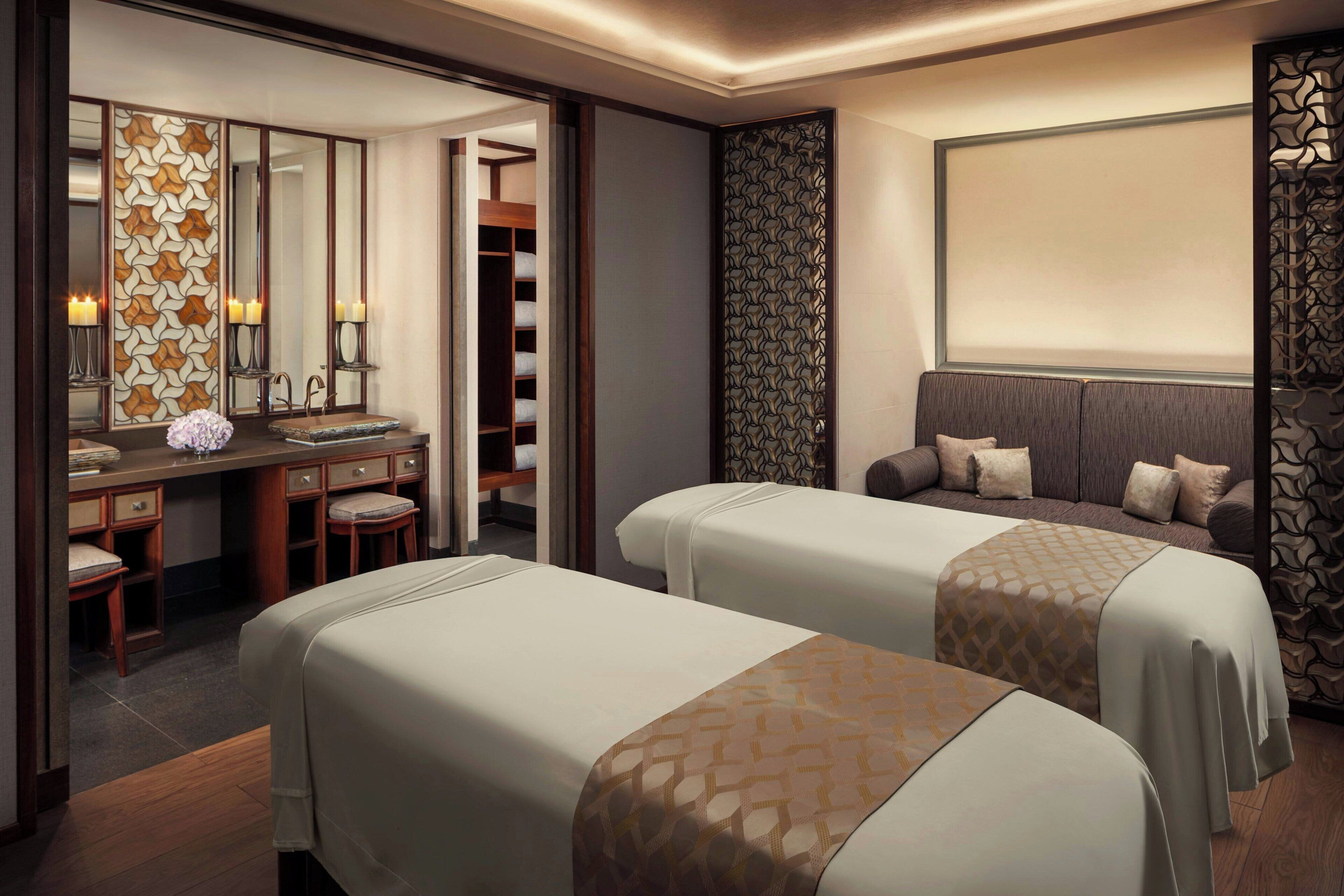 A hotel room with two beds, a desk with a mirror, a vanity, and a large window.