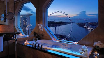 A luxurious bathroom with a large bathtub, a vanity with a mirror, and a view of a Ferris wheel and cityscape.