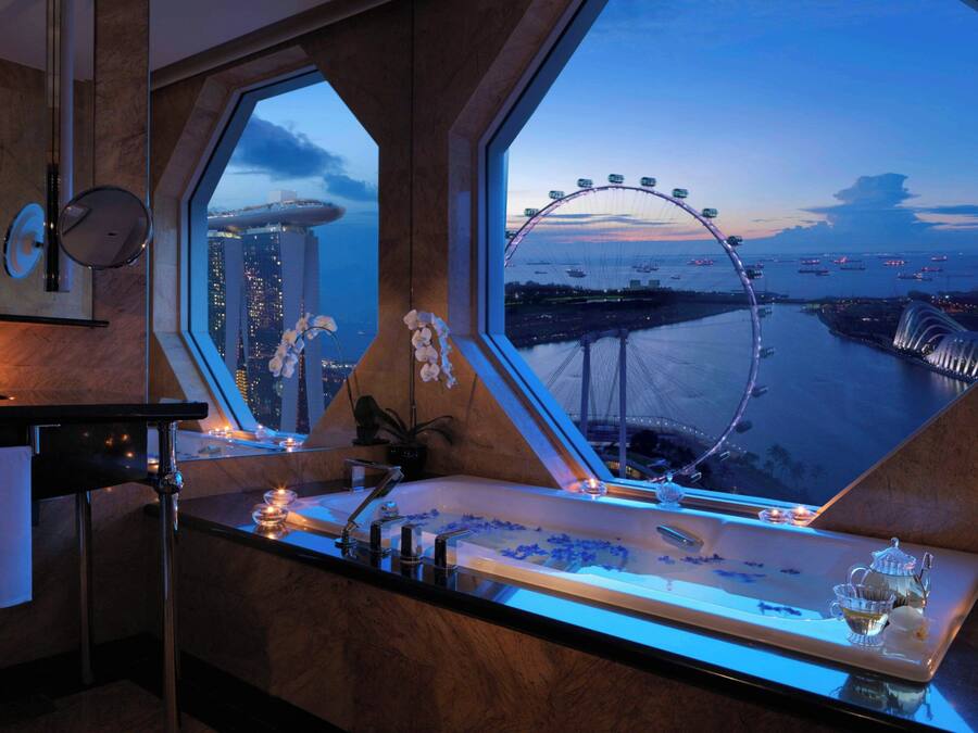 A luxurious bathroom with a large bathtub, a vanity with a mirror, and a view of a Ferris wheel and cityscape.