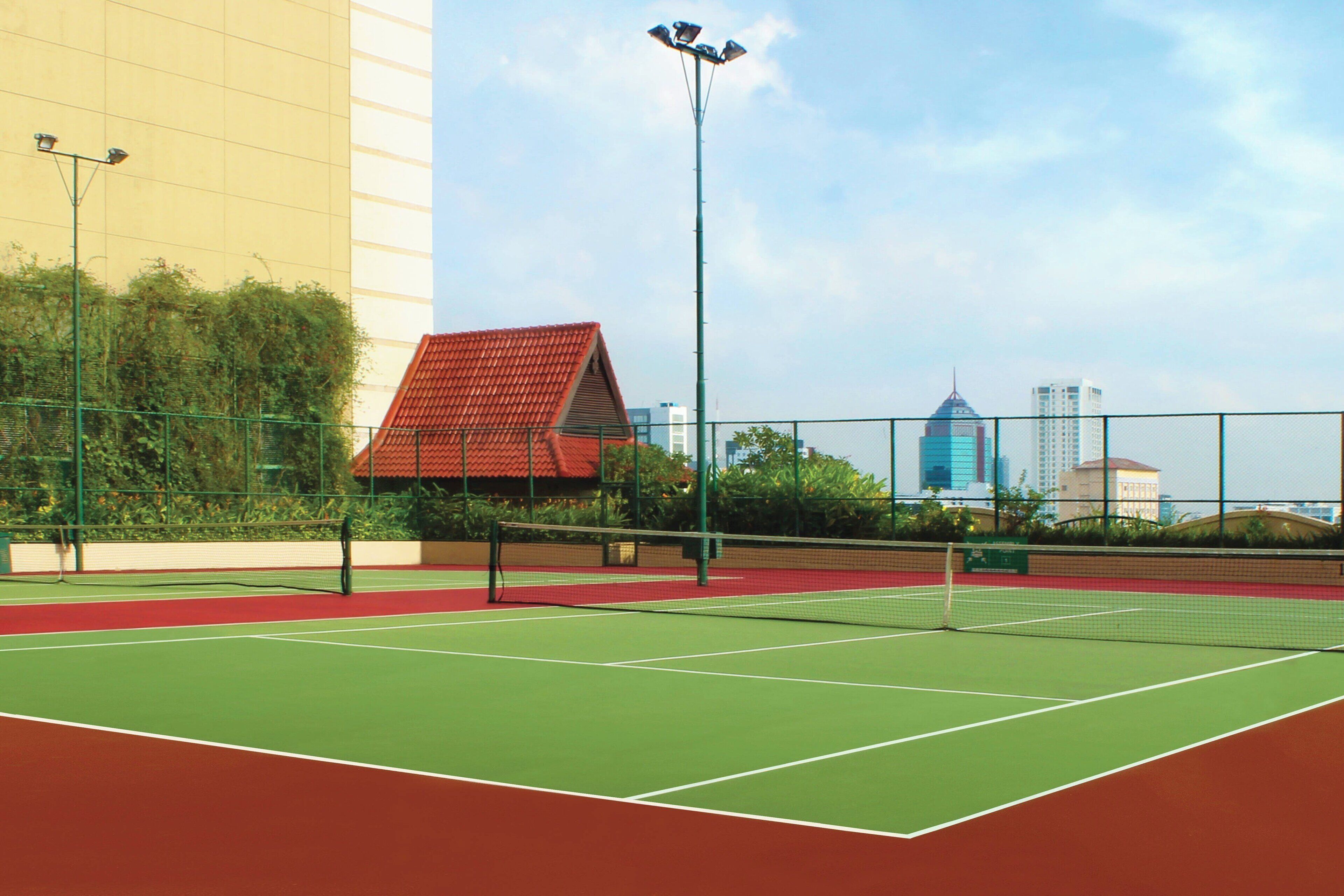 Cancha de tenis exterior con red, rodeada por una cerca y follaje.