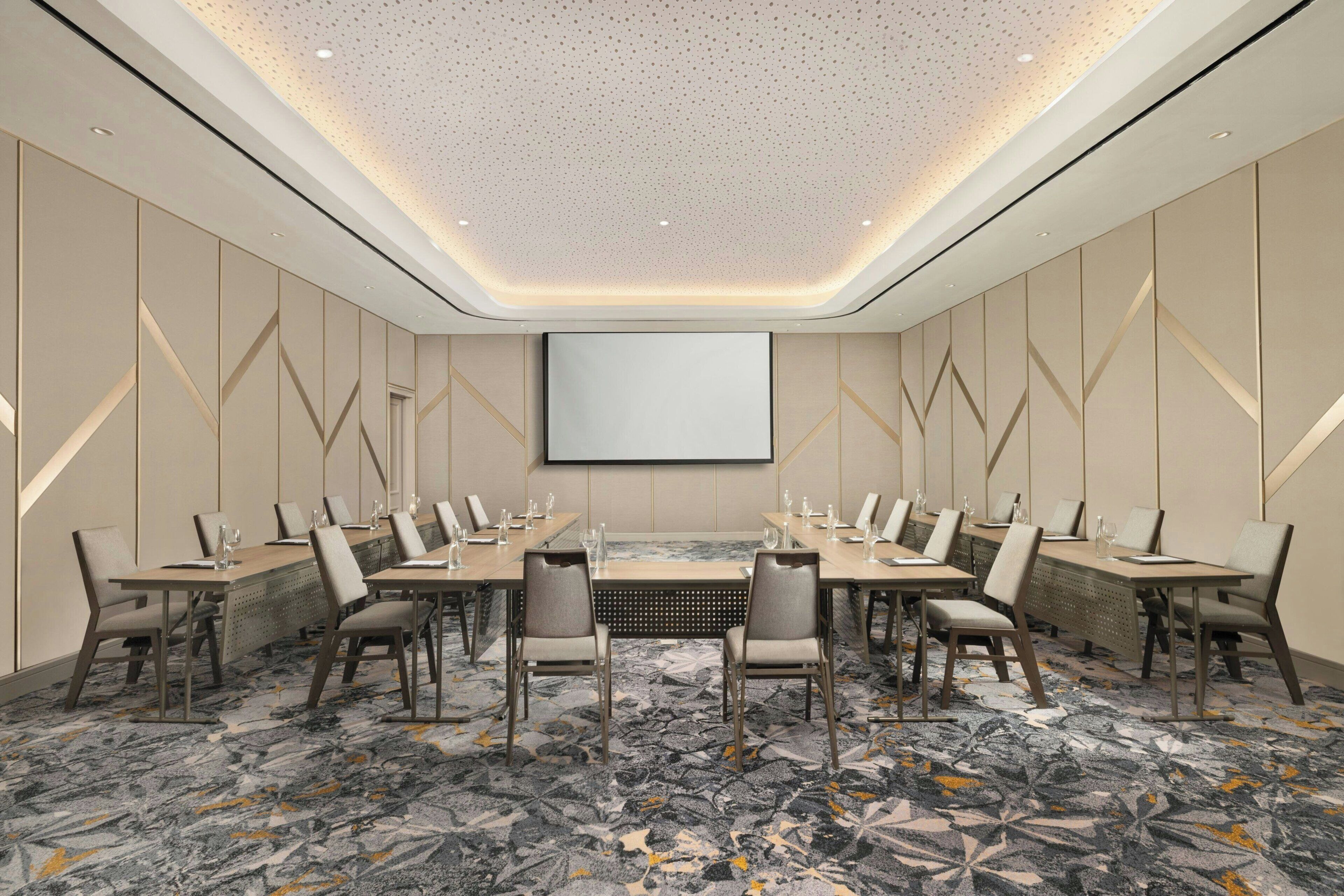 A conference room with a large screen, long tables, and chairs.