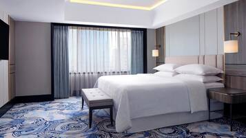 A modern hotel room with a large bed, a bench, a bedside table, and a large window with curtains.