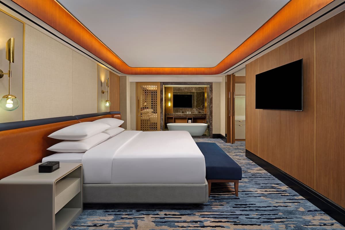Une chambre d’hôtel moderne dotée d’un grand lit, d’une télévision à écran plat, d’une baignoire intégrée et d’un mur décoratif en bois.