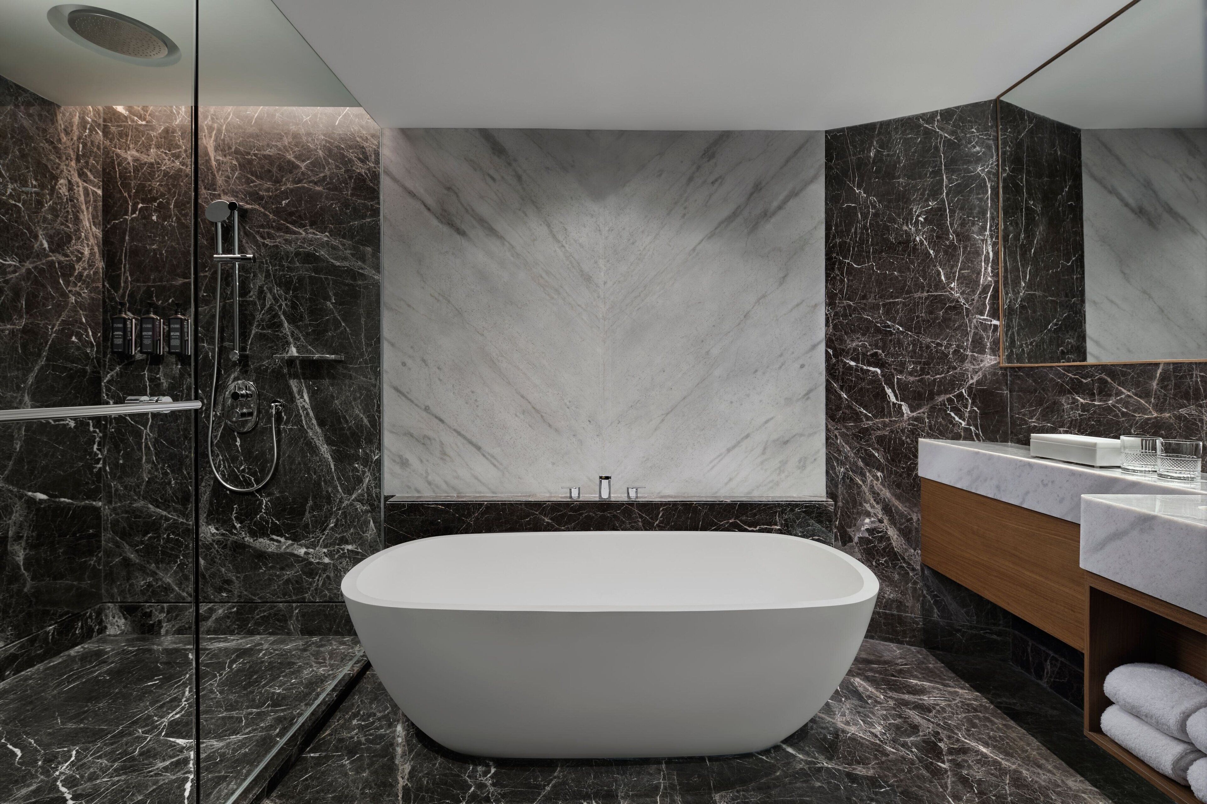 A modern bathroom with a freestanding bathtub, a glass-enclosed shower, and a marble wall.