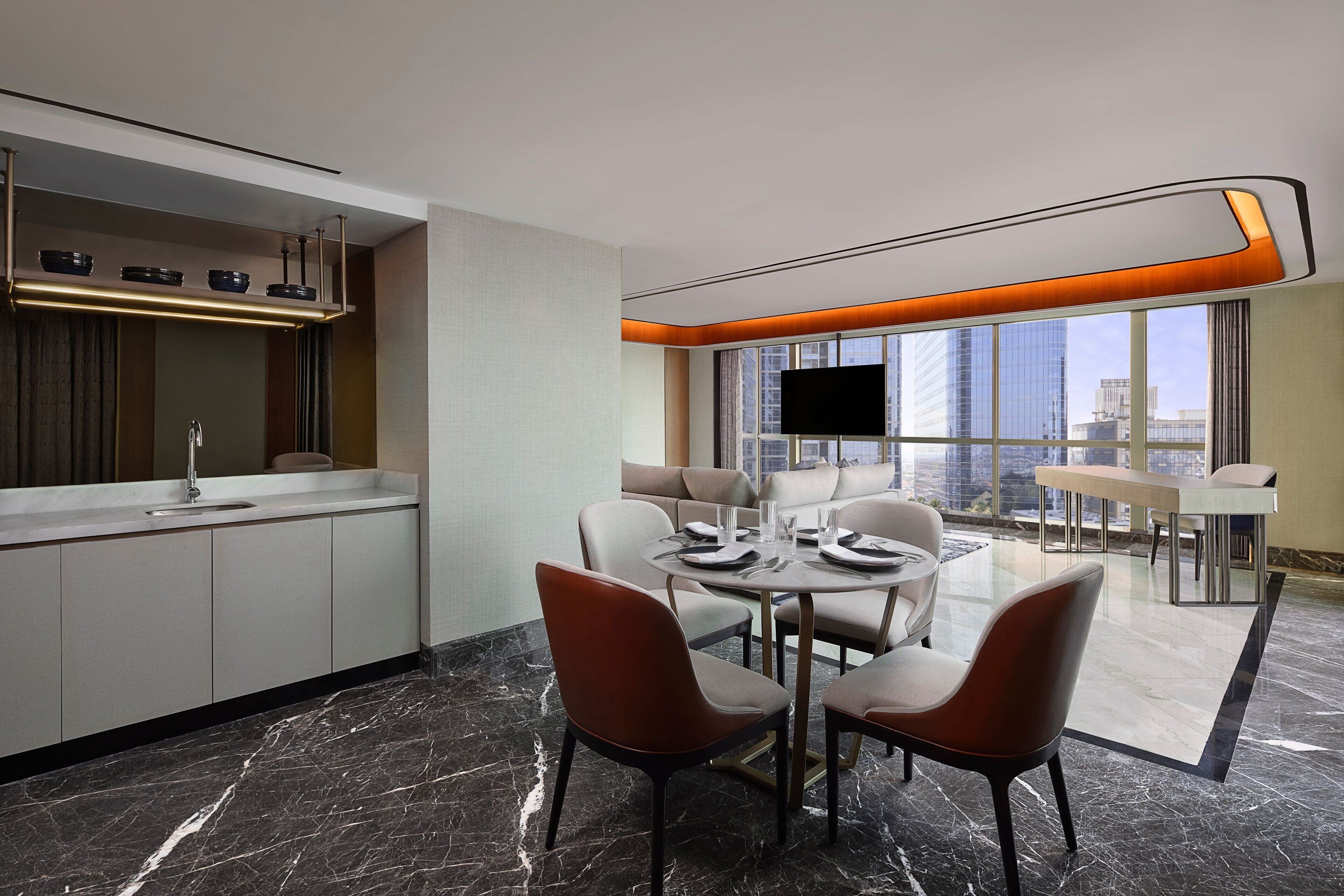 Een moderne hotelkamer met een zithoek, een keuken met een ingebouwde oven, een groot raam met uitzicht over de stad en een wandgemonteerde flatscreen-tv.