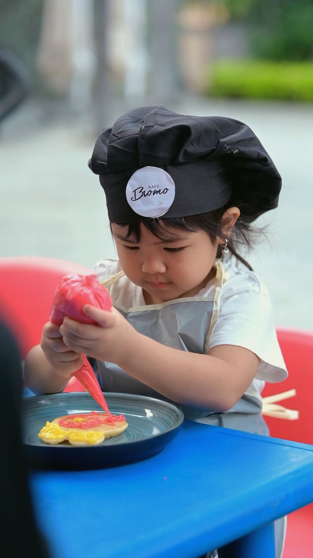 A child wearing a chef's hat and apron, sitting at a table with a plate of food.