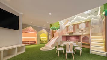 A children's play area with a slide, play tables, and a TV screen.