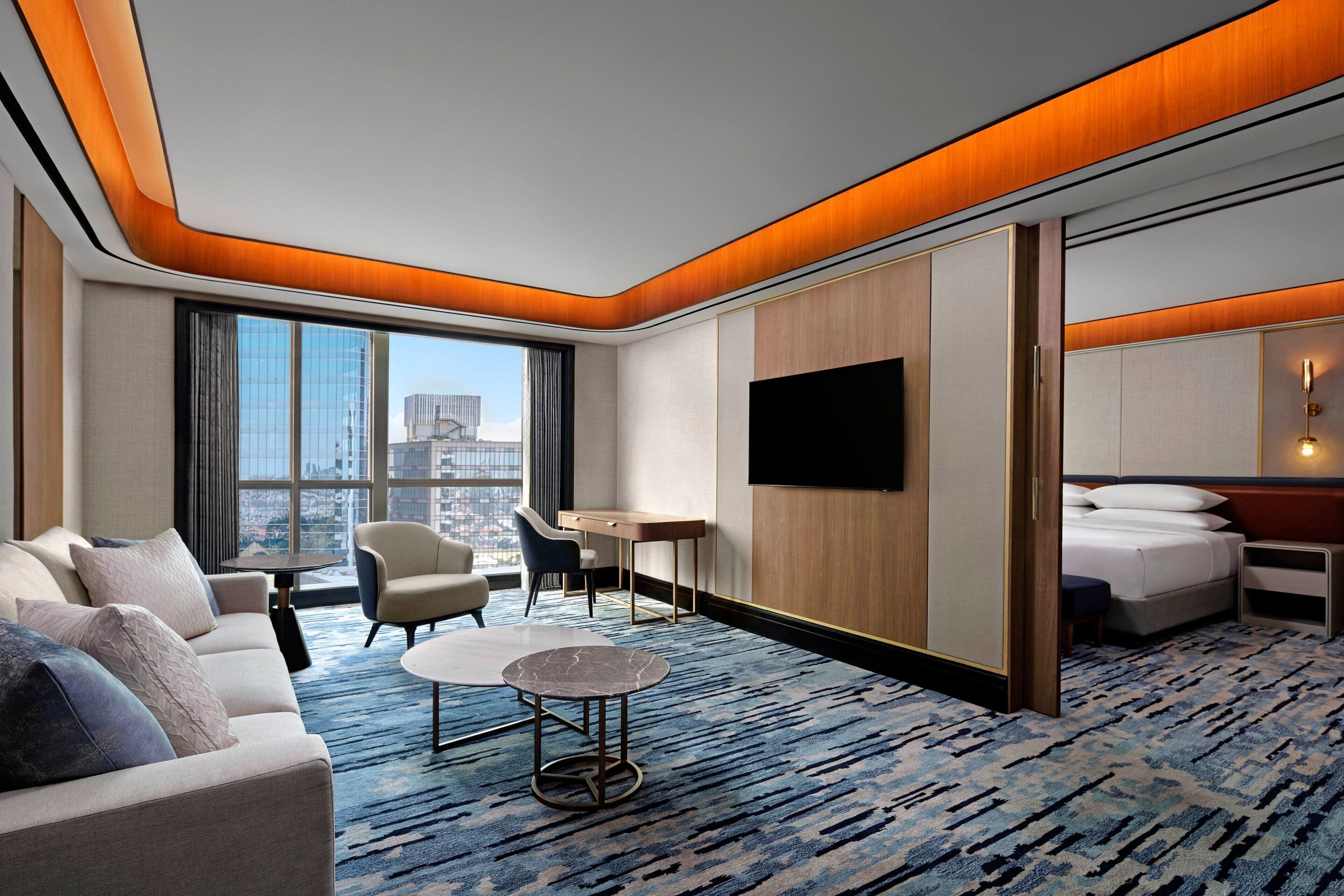A modern hotel room with a large bed, a sofa, a desk, and a TV.