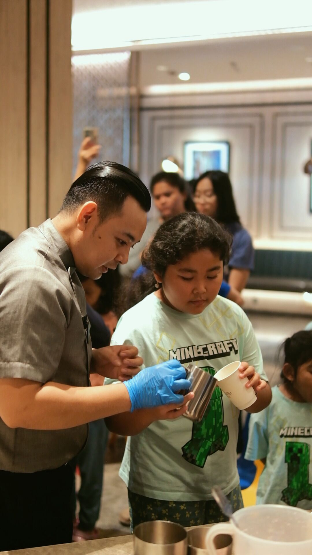 A man and a child in a casual setting, possibly a hotel lobby, with a focus on a person holding a cup and a metal container.