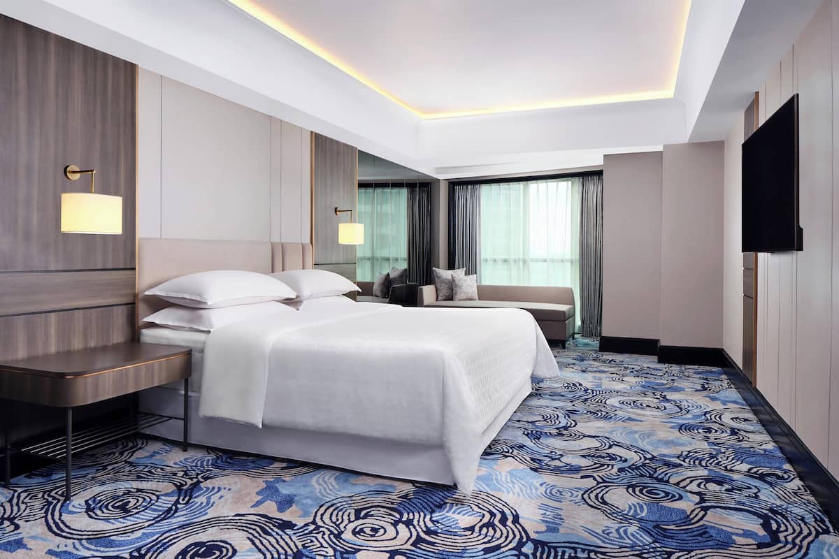 Une chambre d’hôtel moderne dotée d’un grand lit, de tables de chevet, d’un téléviseur à écran plat et d’une moquette à motifs.