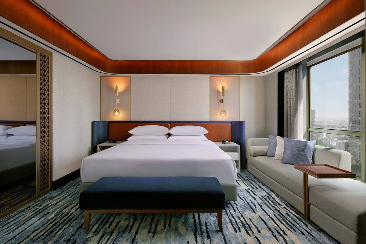 Une chambre d’hôtel avec un grand lit, un canapé, un banc et une petite table.