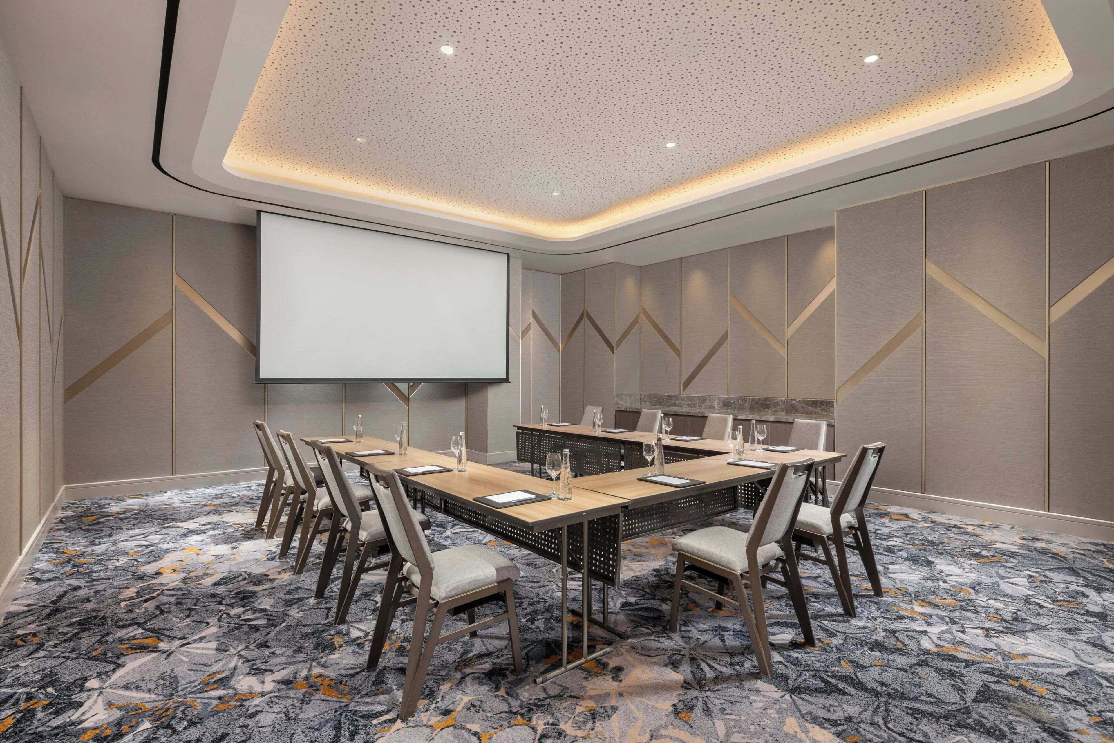 Une salle de conférence avec une longue table, des chaises, un écran de projection et une moquette à motifs.