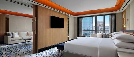 A modern hotel room with a large bed, a sofa, a TV, and a city view.