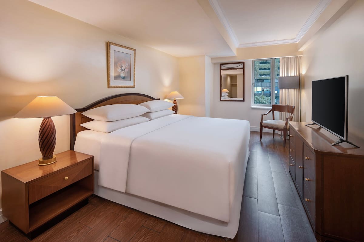 Une chambre d’hôtel avec un grand lit, des lampes de chevet, une table de chevet en bois, une télévision et une chaise.